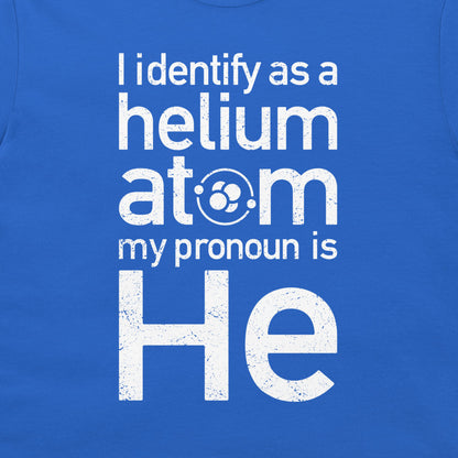 A close-up of a blue T-shirt or fabric panel with large distressed white text reading, 'I identify as a helium atom my pronoun is He.' The word 'atom' includes a small circular atom graphic inside the 'o.