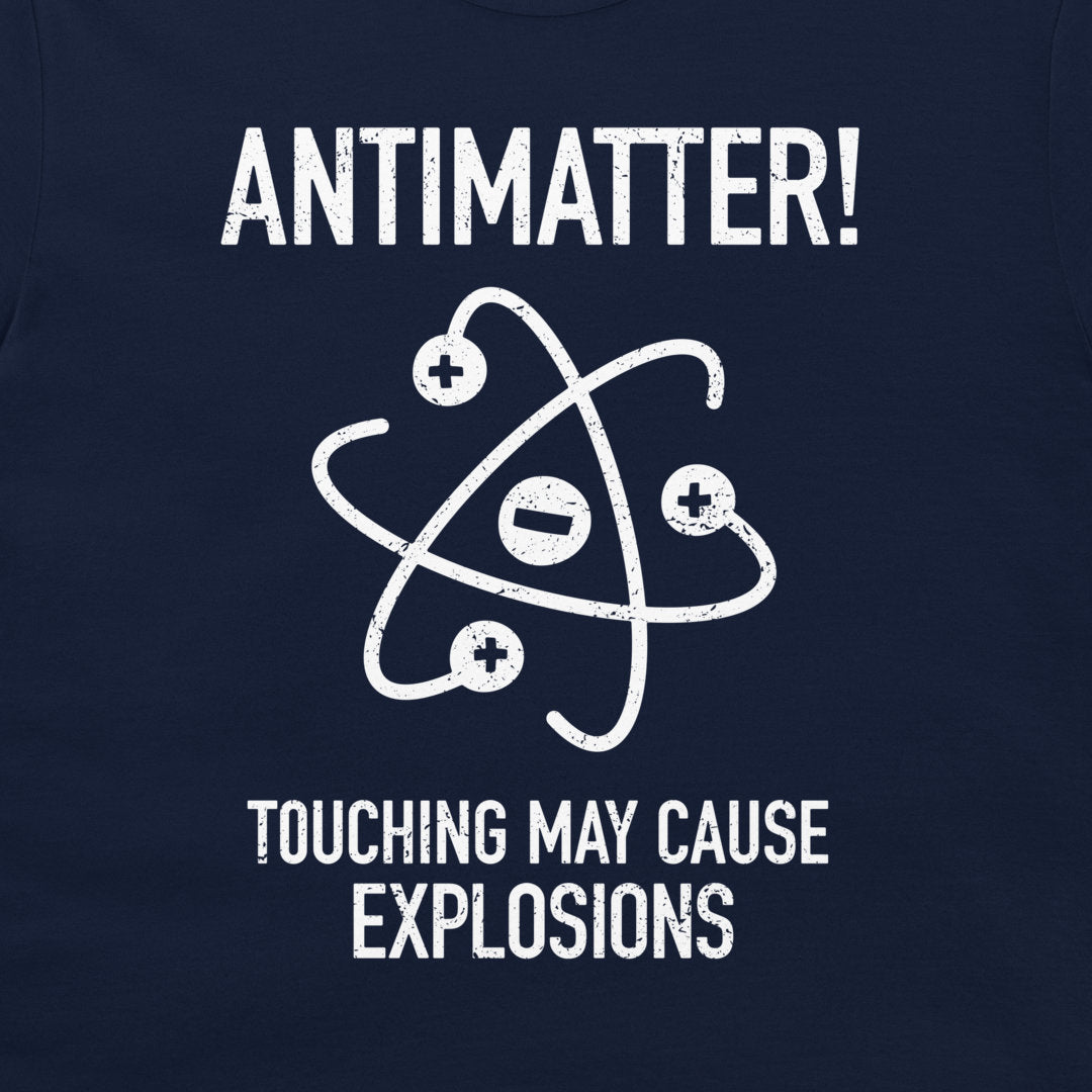 A close-up of a dark navy blue t-shirt featuring a white distressed graphic of an atom with plus and minus signs, accompanied by the text 'ANTIMATTER! TOUCHING MAY CAUSE EXPLOSIONS'.