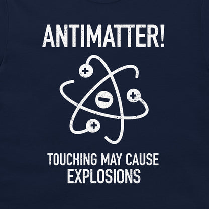 A close-up of a dark navy blue t-shirt featuring a white distressed graphic of an atom with plus and minus signs, accompanied by the text 'ANTIMATTER! TOUCHING MAY CAUSE EXPLOSIONS'.