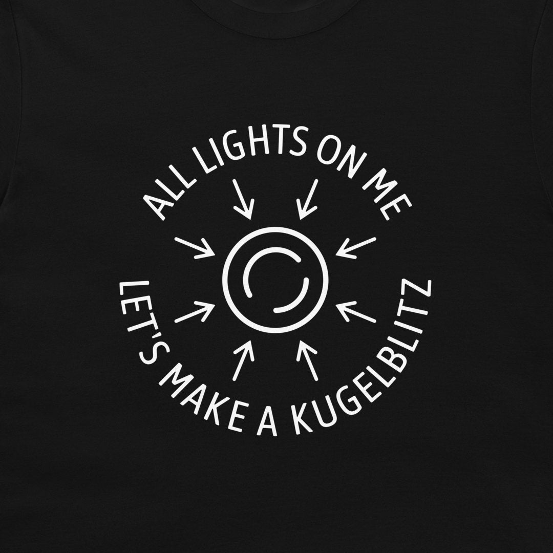 A close-up of a black t-shirt, featuring a white circular graphic with arrows radiating from a central symbol and the text 'ALL LIGHTS ON ME LET'S MAKE A KUGELBLITZ'.