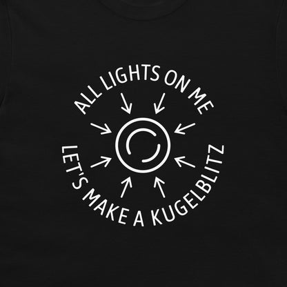A close-up of a black t-shirt, featuring a white circular graphic with arrows radiating from a central symbol and the text 'ALL LIGHTS ON ME LET'S MAKE A KUGELBLITZ'.