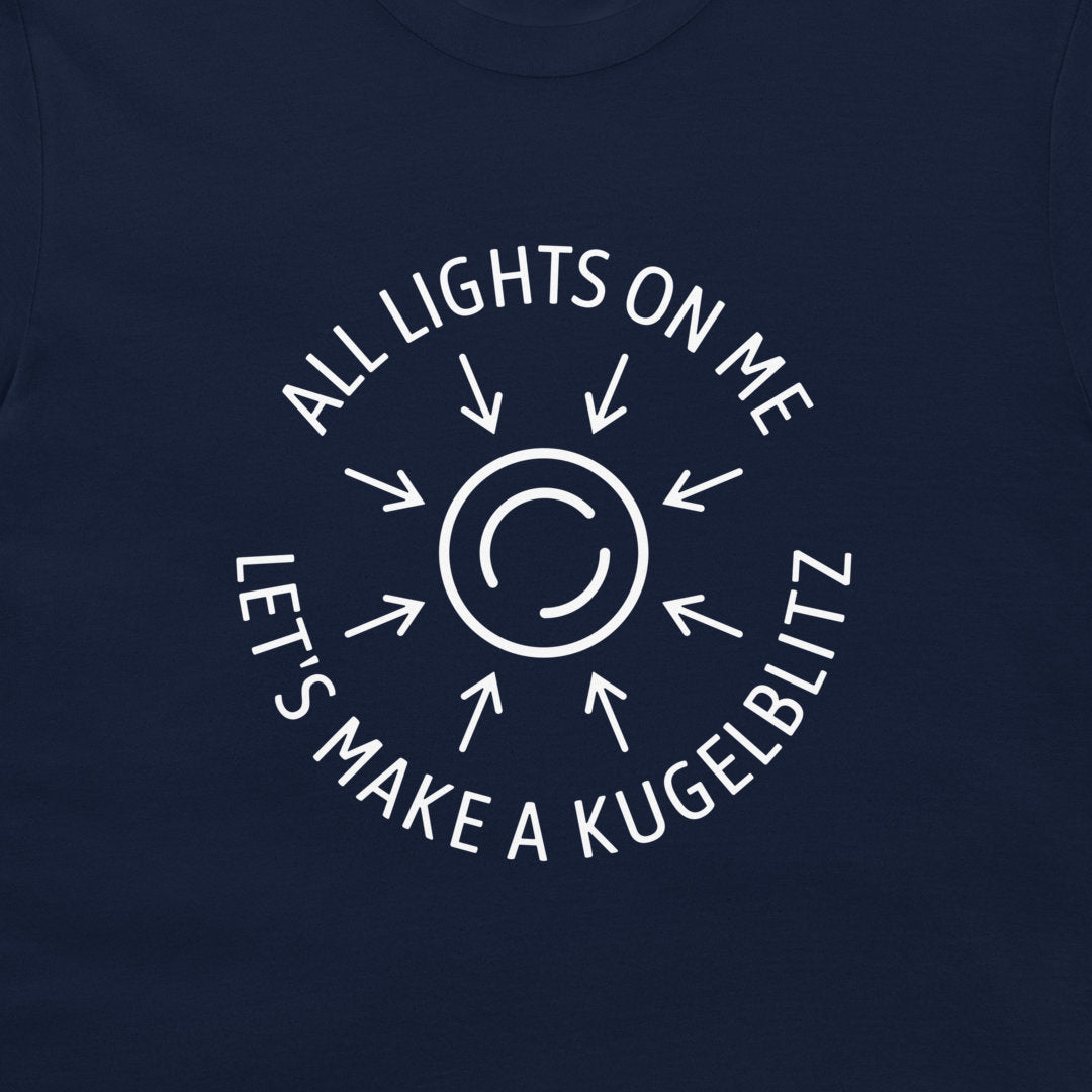 A close-up of a navy blue t-shirt, featuring a white circular graphic with arrows and the text 'ALL LIGHTS ON ME LET'S MAKE A KUGELBLITZ'.