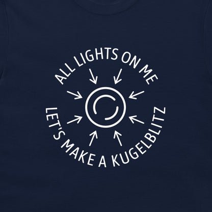 A close-up of a navy blue t-shirt, featuring a white circular graphic with arrows and the text 'ALL LIGHTS ON ME LET'S MAKE A KUGELBLITZ'.