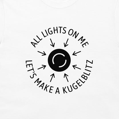 A close-up of a white t-shirt, featuring a black circular graphic with the text 'ALL LIGHTS ON ME LET'S MAKE A KUGELBLITZ' and arrows radiating from a central black circle.
