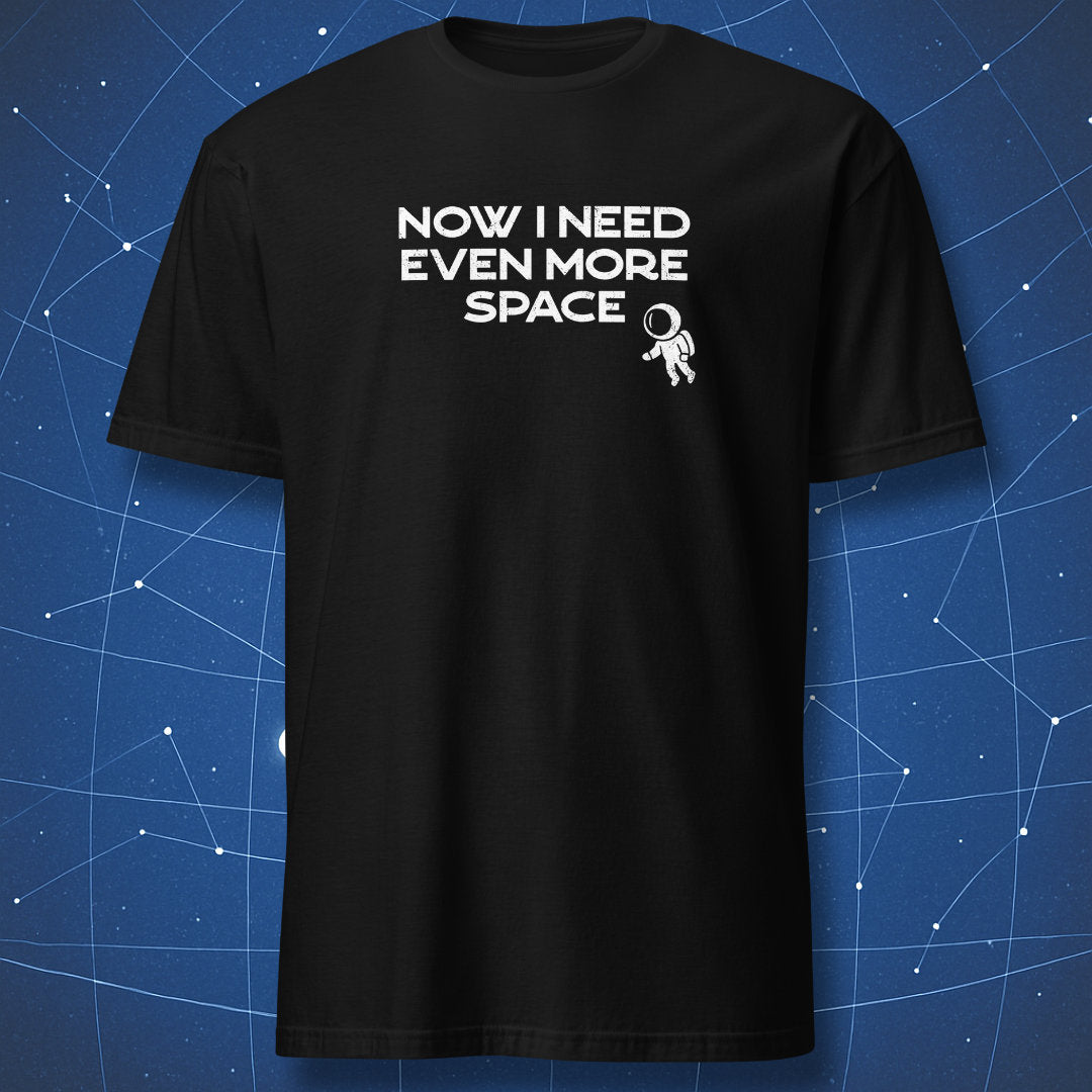 Black t-shirt with 'NOW I NEED EVEN MORE SPACE' text and astronaut graphic on a blue grid background. A cosmic nerd tee from DorkMatter