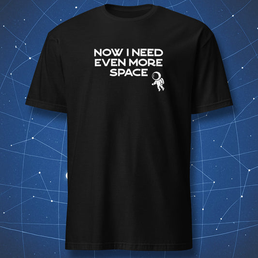 Black t-shirt with 'NOW I NEED EVEN MORE SPACE' text and astronaut graphic on a blue grid background. A cosmic nerd tee from DorkMatter