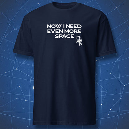 Navy blue t-shirt with 'Now I need even more space' text and astronaut graphic on a starry night sky background.  A cosmic nerd tee from DorkMatter.