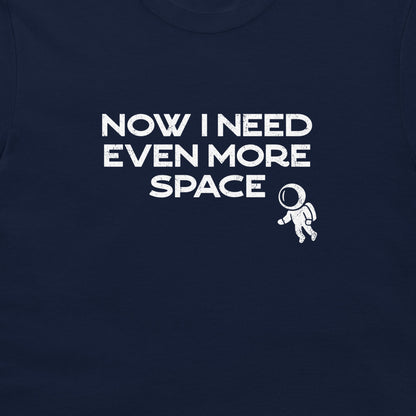 A close-up of a navy blue t-shirt featuring a white graphic print that reads 'NOW I NEED EVEN MORE SPACE' next to a small astronaut illustration.
