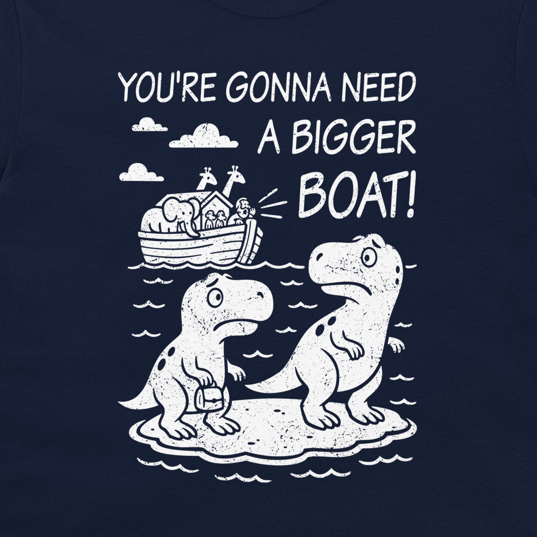 A navy blue t-shirt featuring a white graphic print of two dinosaurs sitting on a rock, with Noah's Ark in the background and the text 'YOU'RE GONNA NEED A BIGGER BOAT!'.
