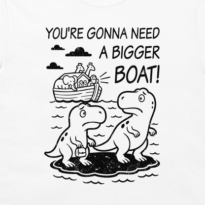 A close-up of a white t-shirt featuring a black graphic print. The design shows two cartoon dinosaurs standing on a small island, with Noah's Ark depicted in the background under clouds and the text 'YOU'RE GONNA NEED A BIGGER BOAT!'.