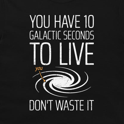 A close-up of a black graphic t-shirt featuring a white distressed text design that reads 'YOU HAVE 10 GALACTIC SECONDS TO LIVE DON'T WASTE IT' with a white spiral galaxy illustration and a small orange arrow pointing to the word 'you'.
