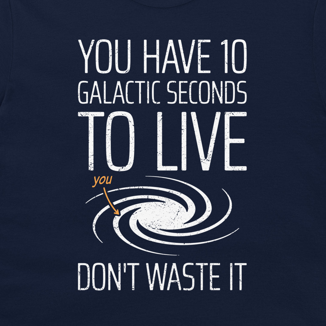 A close-up of a navy blue t-shirt featuring a white distressed graphic that reads 'YOU HAVE 10 GALACTIC SECONDS TO LIVE DON'T WASTE IT' with a spiral galaxy illustration and a small orange arrow pointing to the word 'you'.