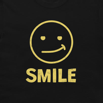 A close-up of a black t-shirt, featuring a distressed yellow graphic of a smiling face with the word 'SMILE' printed below it.
