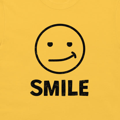 A close-up of a yellow t-shirt, featuring a black distressed graphic of a simple smiley face with the word 'SMILE' printed below it.