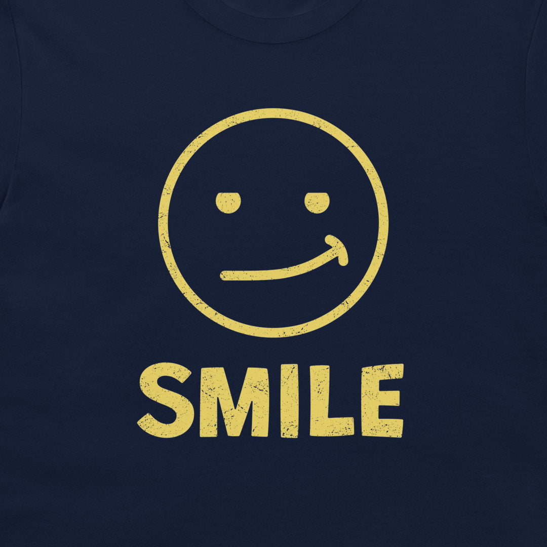 A close-up of a navy blue t-shirt featuring a distressed yellow graphic of a smiling face with the word 'SMILE' printed below it.