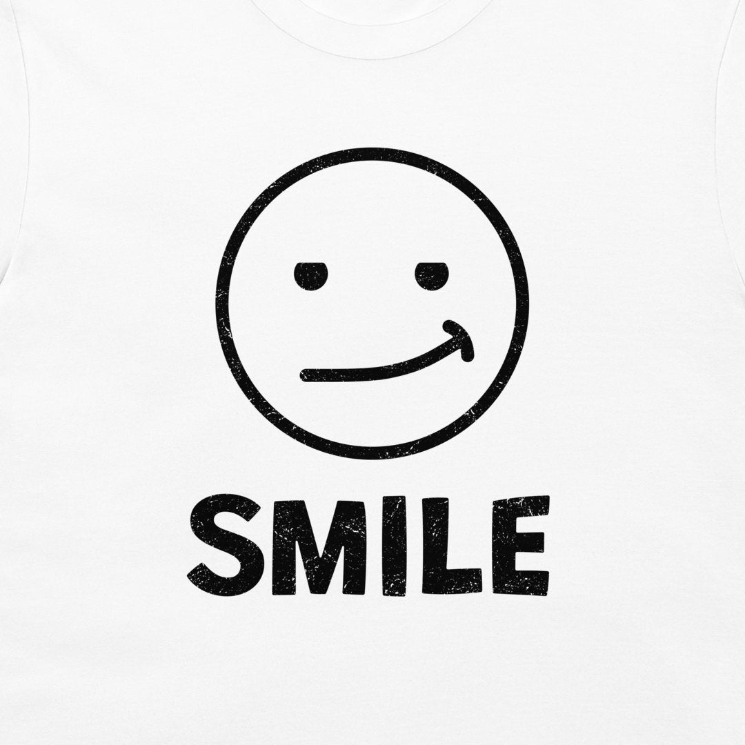 White t-shirt featuring a black distressed graphic of a simple smiley face with the word 'SMILE' printed underneath.