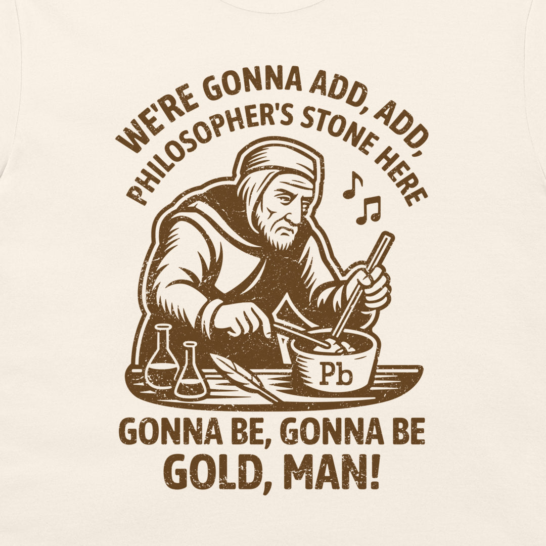 A close-up of a cream-colored  t-shirt, featuring a dark brown graphic print of an alchemist mixing chemicals with the text 'WE'RE GONNA ADD, ADD, PHILOSOPHER'S STONE HERE' and 'GONNA BE, GONNA BE GOLD, MAN!'.