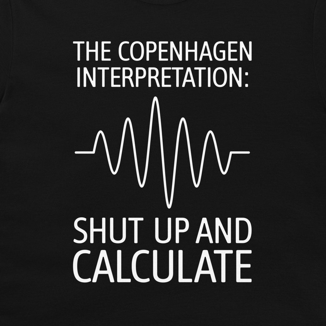 A close-up of a black t-shirt, featuring a white graphic print that reads 'THE COPENHAGEN INTERPRETATION: SHUT UP AND CALCULATE' with a white heartbeat-style waveform line in the center.