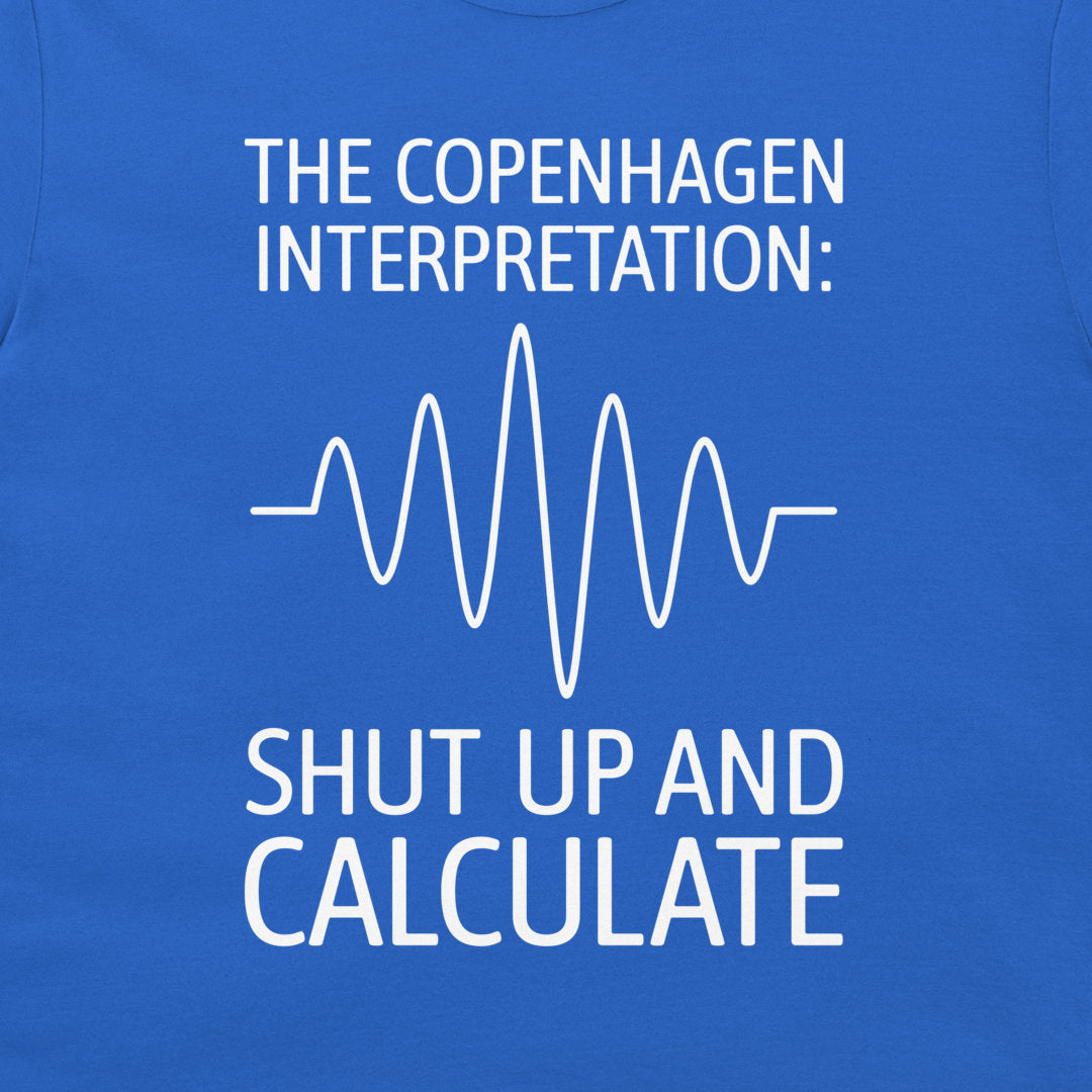 A close-up of a blue T-shirt with white printed text reading 'THE COPENHAGEN INTERPRETATION:' above a white waveform line and 'SHUT UP AND CALCULATE' below.