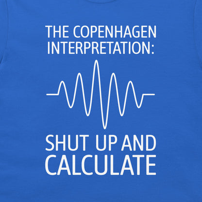 A close-up of a blue T-shirt with white printed text reading 'THE COPENHAGEN INTERPRETATION:' above a white waveform line and 'SHUT UP AND CALCULATE' below.