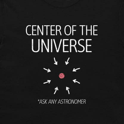 A close-up of a black t-shirt featuring a white graphic print that reads 'CENTER OF THE UNIVERSE' with arrows pointing toward a small pink dot, and the text '*ASK ANY ASTRONOMER' below.