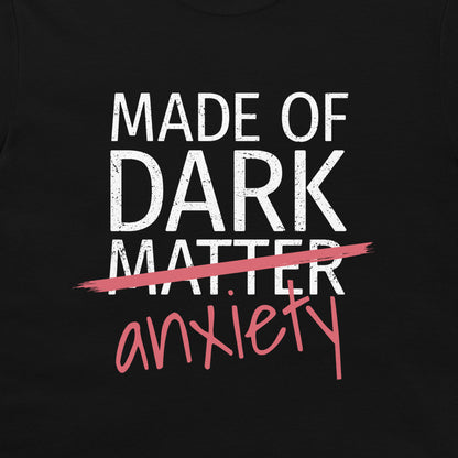 A close-up of a black graphic print on a shirt or garment. The design reads 'MADE OF DARK MATTER' in distressed white block letters, crossed out with a pink brushstroke, with 'anxiety' written below in pink script.