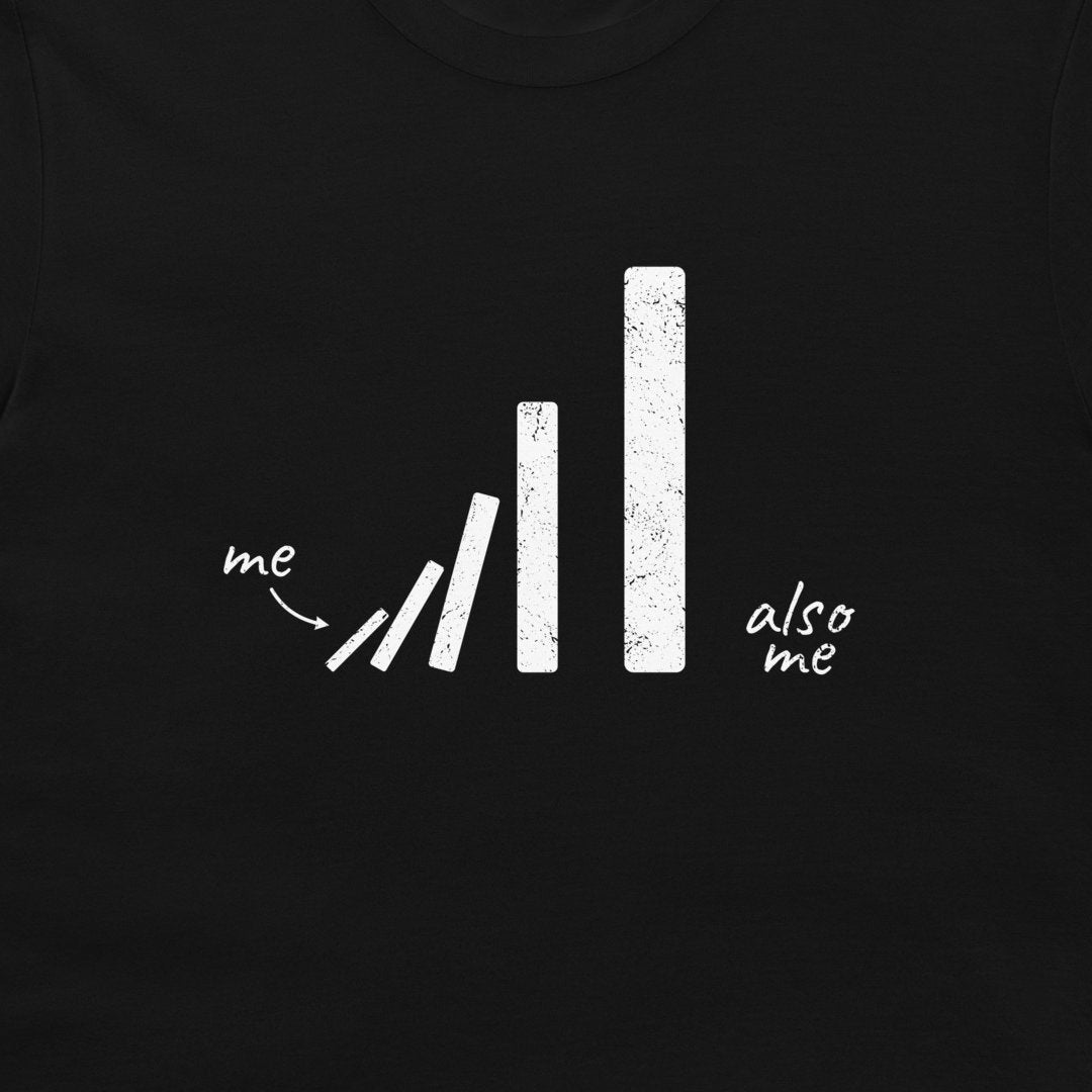 A close-up of a black garment, likely a t-shirt, featuring a white distressed graphic of falling dominoes with the words 'me' and 'also me' written in a handwritten font.