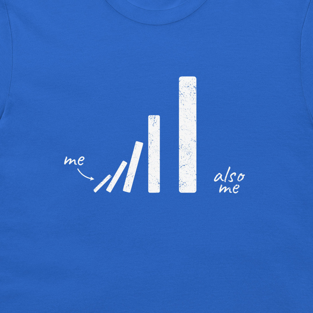 A close-up of a royal blue t-shirt featuring a white distressed graphic of falling dominoes with the handwritten words 'me' and 'also me'.