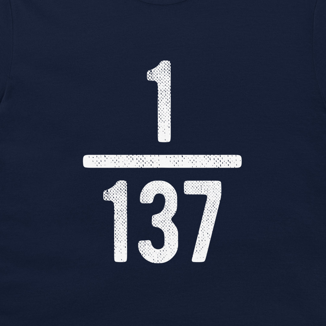 A close-up of a navy blue t-shirt, featuring a large white distressed graphic of the fraction 1/137 on the chest.