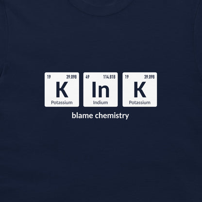 A close-up of a navy blue t-shirt featuring a white graphic print of three periodic table tiles spelling 'K In K' with the text 'blame chemistry' underneath.