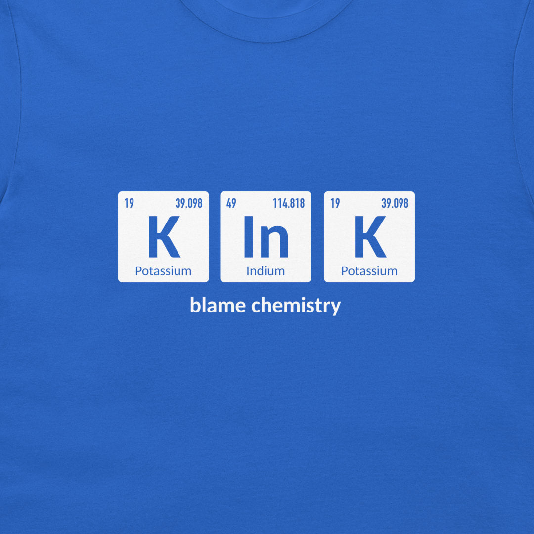 A close-up of a bright blue crewneck t-shirt featuring a graphic print of three white periodic table tiles spelling 'K In K' with the text 'blame chemistry' underneath.