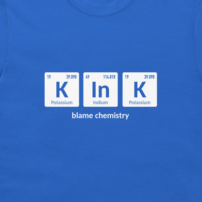 A close-up of a bright blue crewneck t-shirt featuring a graphic print of three white periodic table tiles spelling 'K In K' with the text 'blame chemistry' underneath.