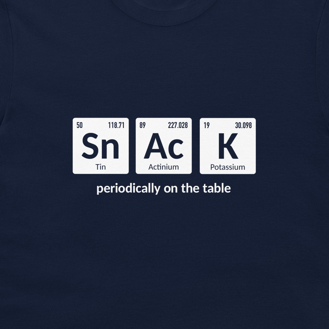 A close-up of a navy blue t-shirt featuring a white graphic of three periodic table tiles spelling 'SnAcK' with the phrase 'periodically on the table' underneath.