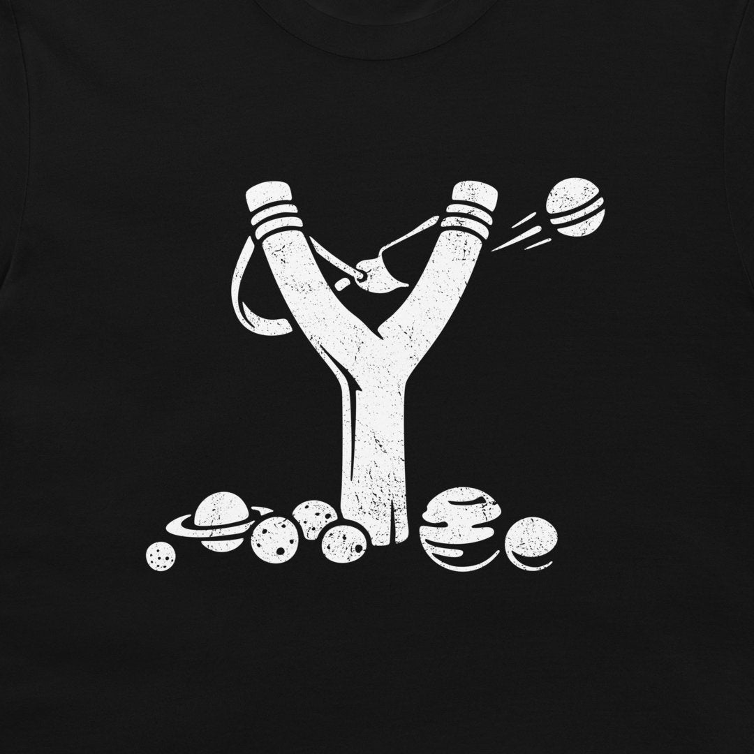 A close-up of a black t-shirt, featuring a distressed white graphic of a slingshot launching planets.