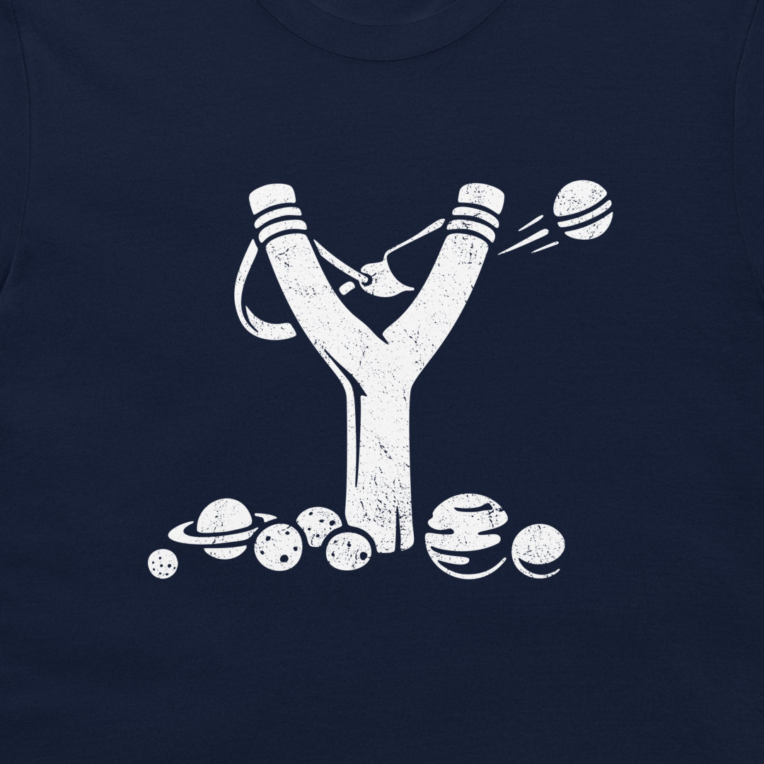 A close-up of a navy blue t-shirt, featuring a distressed white graphic of a slingshot launching planets and moons.
