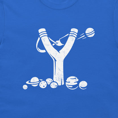 A close-up of a royal blue T-shirt featuring a distressed white graphic of a slingshot launching planets and moons, with several planets and moons illustrated along the bottom.