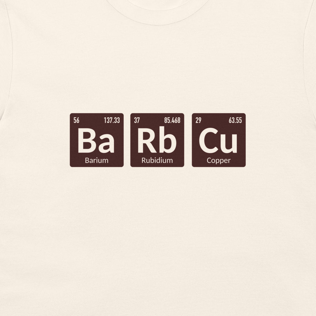 A close-up of a light cream-colored fabric, likely a t-shirt, featuring a graphic of three periodic table elements: Barium (Ba), Rubidium (Rb), and Copper (Cu) in dark brown tiles with white text.