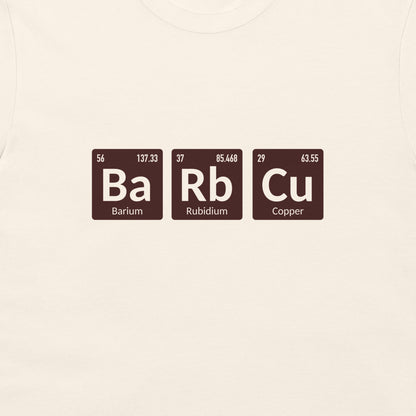 A close-up of a light cream-colored fabric, likely a t-shirt, featuring a graphic of three periodic table elements: Barium (Ba), Rubidium (Rb), and Copper (Cu) in dark brown tiles with white text.