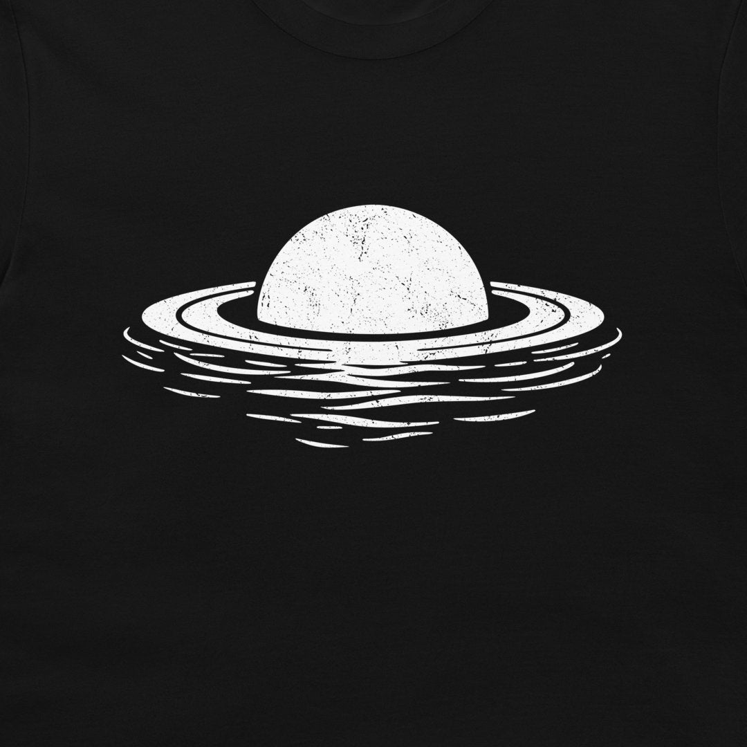 A close-up of a black t-shirt featuring a distressed white graphic of a planet with a ring floating above stylized water ripples.