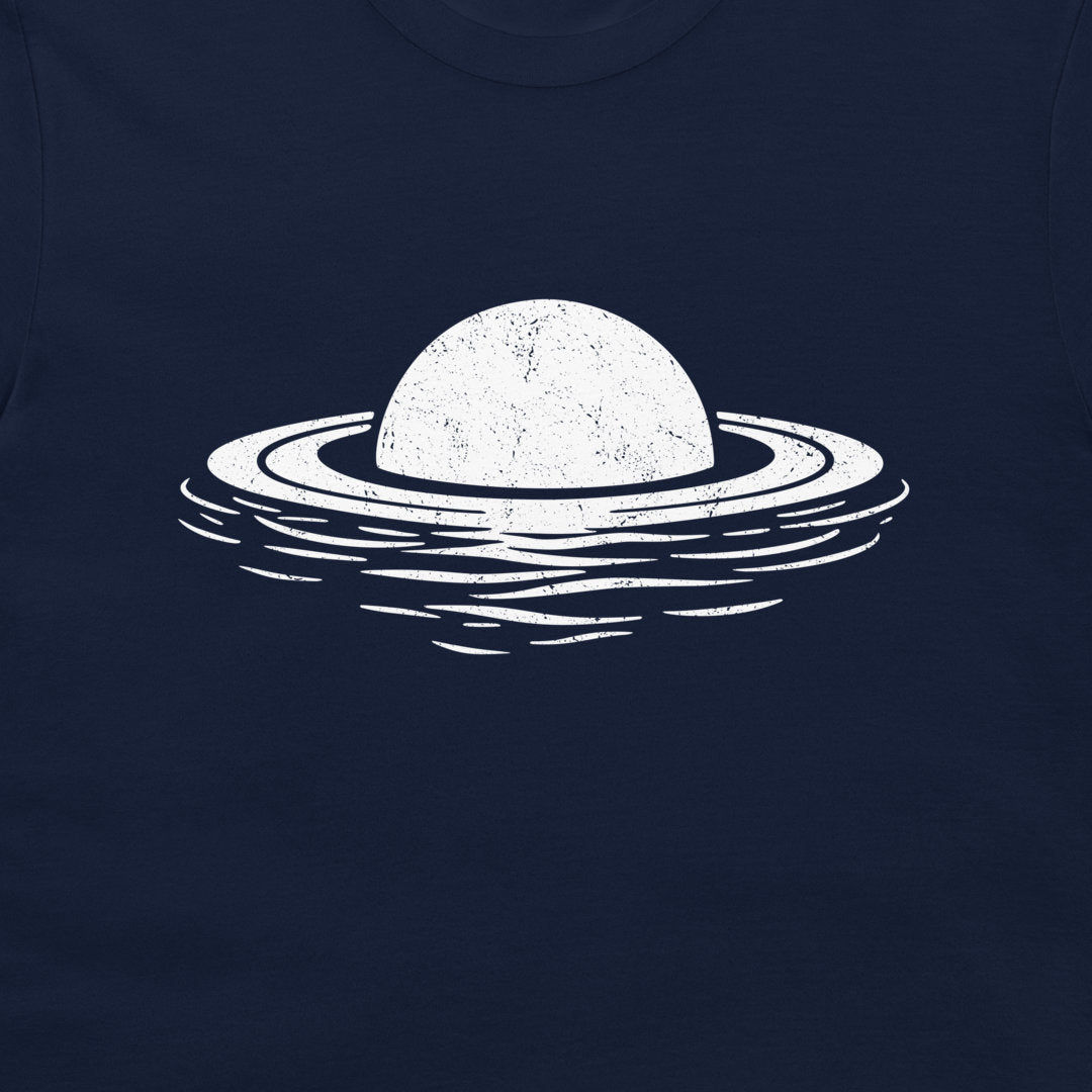 A close-up of a dark navy blue t-shirt featuring a distressed white graphic of a planet with rings floating in water.