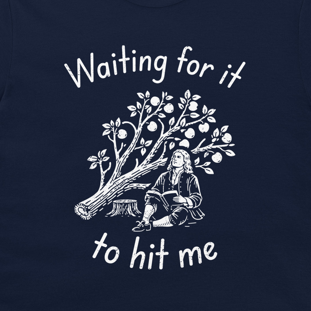 A close-up of a navy blue t-shirt, featuring a white graphic print of a historical figure sitting under an apple tree with the text 'Waiting for it to hit me'.