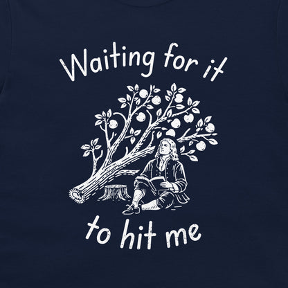 A close-up of a navy blue t-shirt, featuring a white graphic print of a historical figure sitting under an apple tree with the text 'Waiting for it to hit me'.