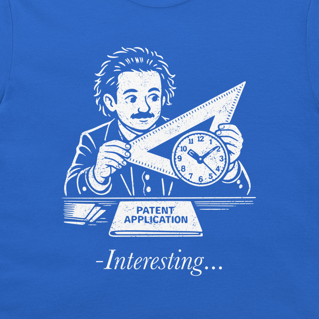 A close-up of a royal blue t-shirt featuring a white graphic print of Albert Einstein holding a triangular ruler and clock, with a banner reading 'PATENT APPLICATION' and the text '-Interesting.
