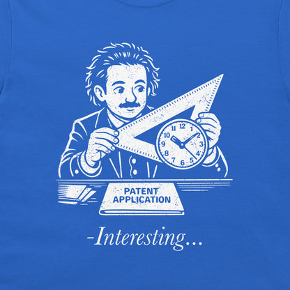 A close-up of a royal blue t-shirt featuring a white graphic print of Albert Einstein holding a triangular ruler and clock, with a banner reading 'PATENT APPLICATION' and the text '-Interesting.