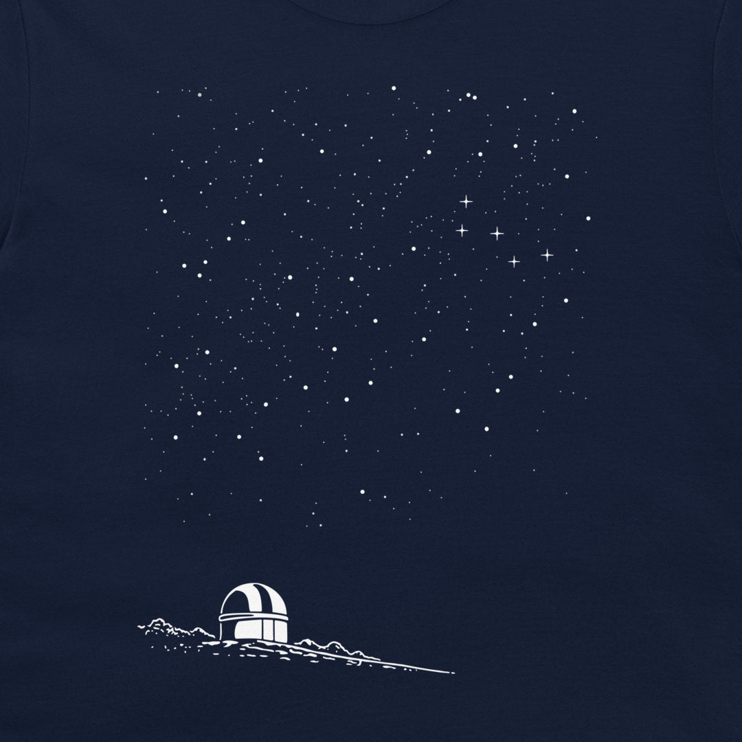 A close-up of a navy blue garment, likely a t-shirt, featuring a white graphic print of a small observatory dome on a mountain ridge beneath a starry night sky.