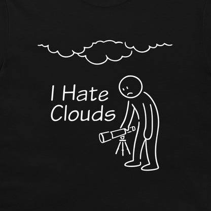 A close-up of a black  t-shirt, featuring a white graphic print. The design shows a stick figure holding a telescope under a cloud, with the text 'I Hate Clouds'.