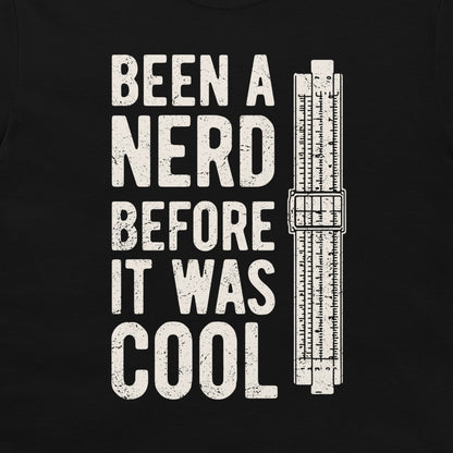 A black t-shirt featuring a distressed white graphic print that reads 'BEEN A NERD BEFORE IT WAS COOL' next to a vintage slide rule measuring device.