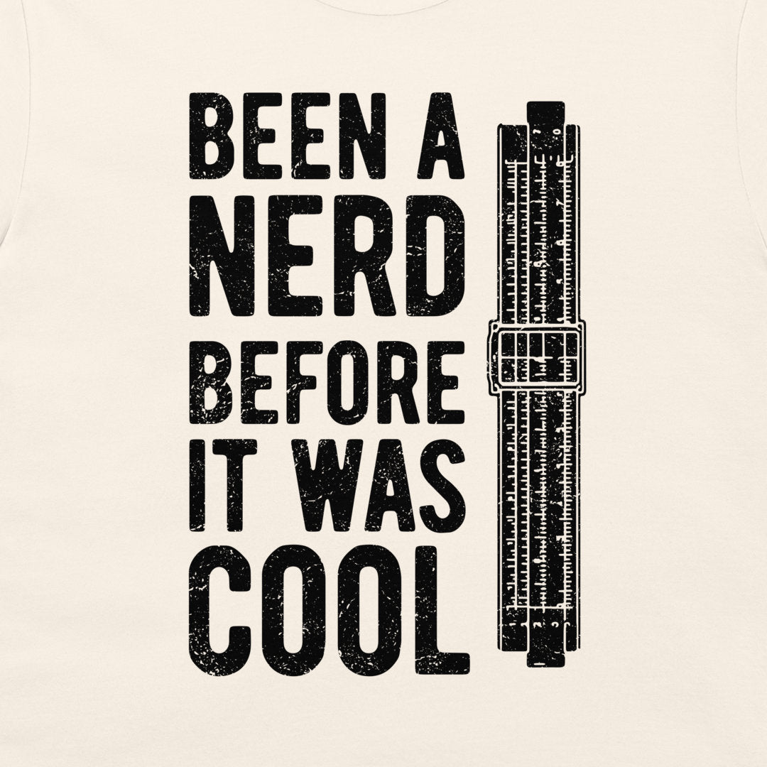 A close-up of an off-white fabric surface with a large black distressed typographic print reading 'BEEN A NERD BEFORE IT WAS COOL' alongside a black vintage slide rule illustration.