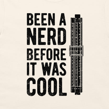 A close-up of an off-white fabric surface with a large black distressed typographic print reading 'BEEN A NERD BEFORE IT WAS COOL' alongside a black vintage slide rule illustration.