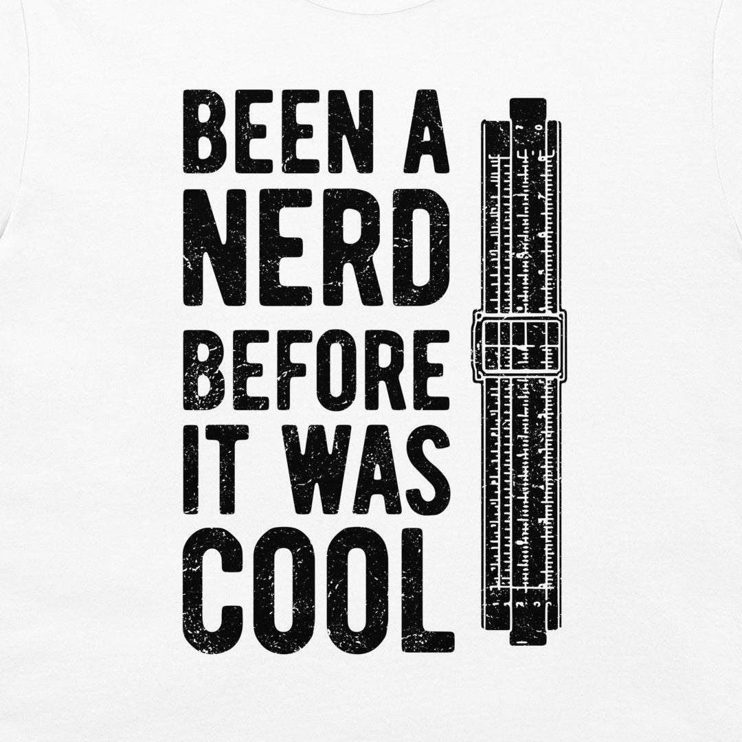 A white t-shirt featuring a bold black graphic print that reads 'BEEN A NERD BEFORE IT WAS COOL' next to an illustration of a vintage slide rule.